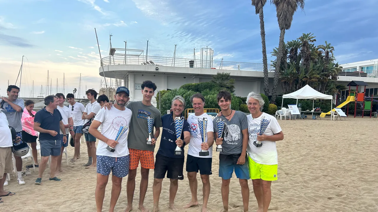 Participantes del PadelBeach 2023 posando en la playa del Maresme al atardecer, con trofeos.